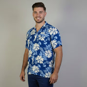 Man wearing a blue floral shirt and beige shorts standing in front of a white backdrop.