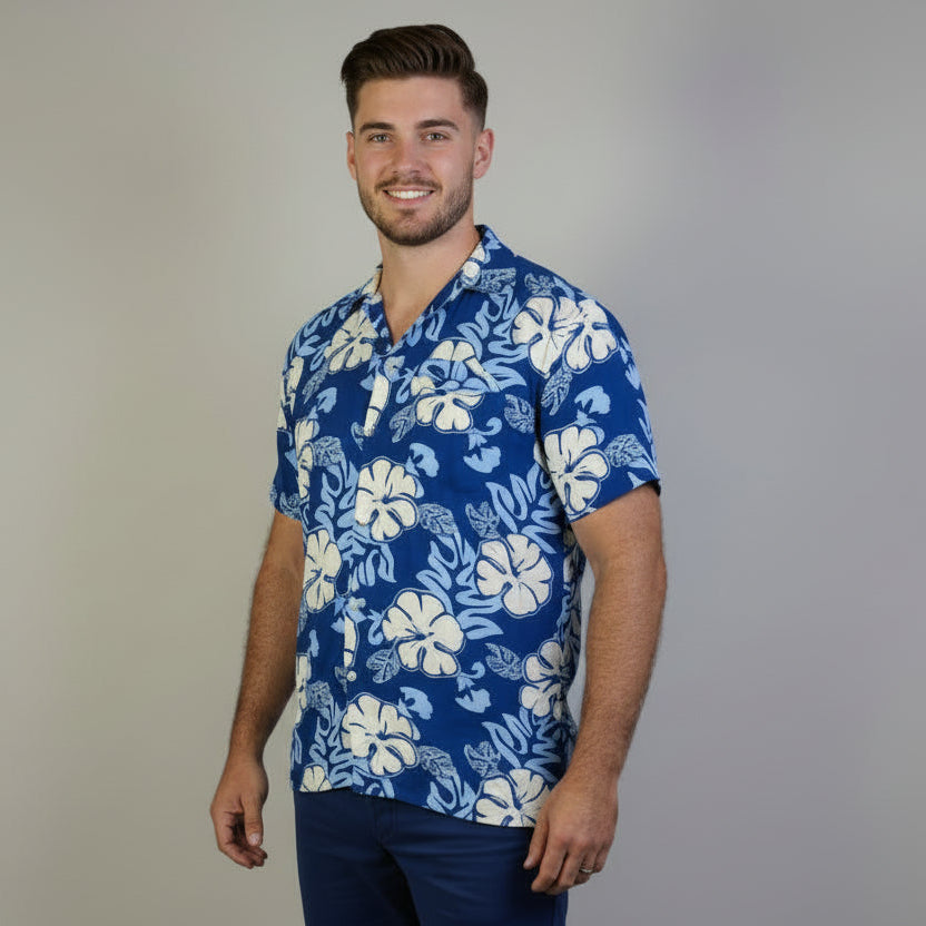 Man wearing a blue floral shirt and beige shorts standing in front of a white backdrop.
