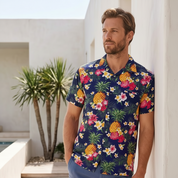 Man wearing a colorful floral shirt and blue shorts standing in a tropical setting.