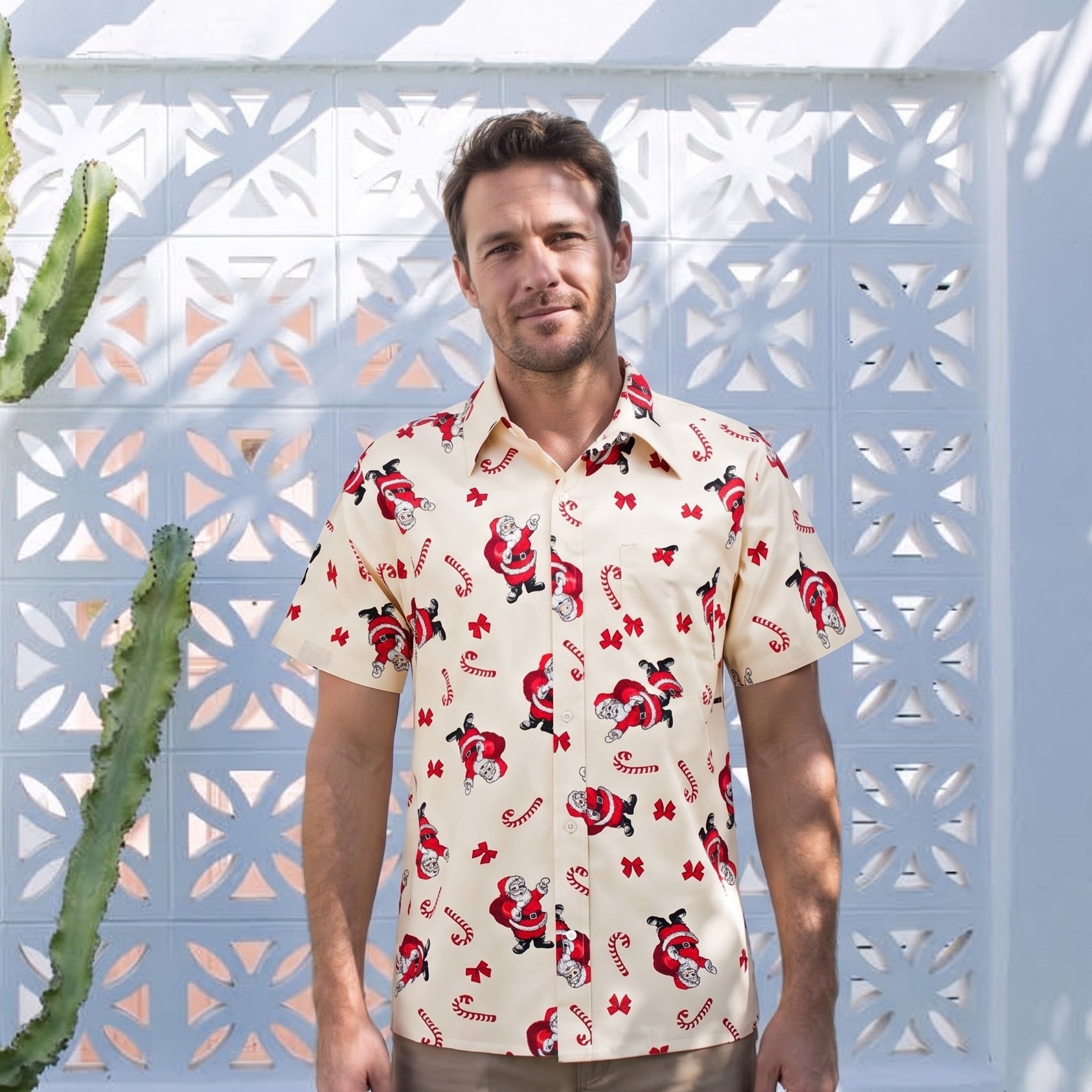 A man wearing a cream-colored short-sleeve button-down shirt with a red and black floral pattern, standing in front of a white geometric wall with a tall green cactus to his left.