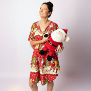 Woman smiling and holding a Santa plush while wearing the Tropicool Happy Santa Red Kaftan. Bright festive print kaftan for Australian Christmas celebrations