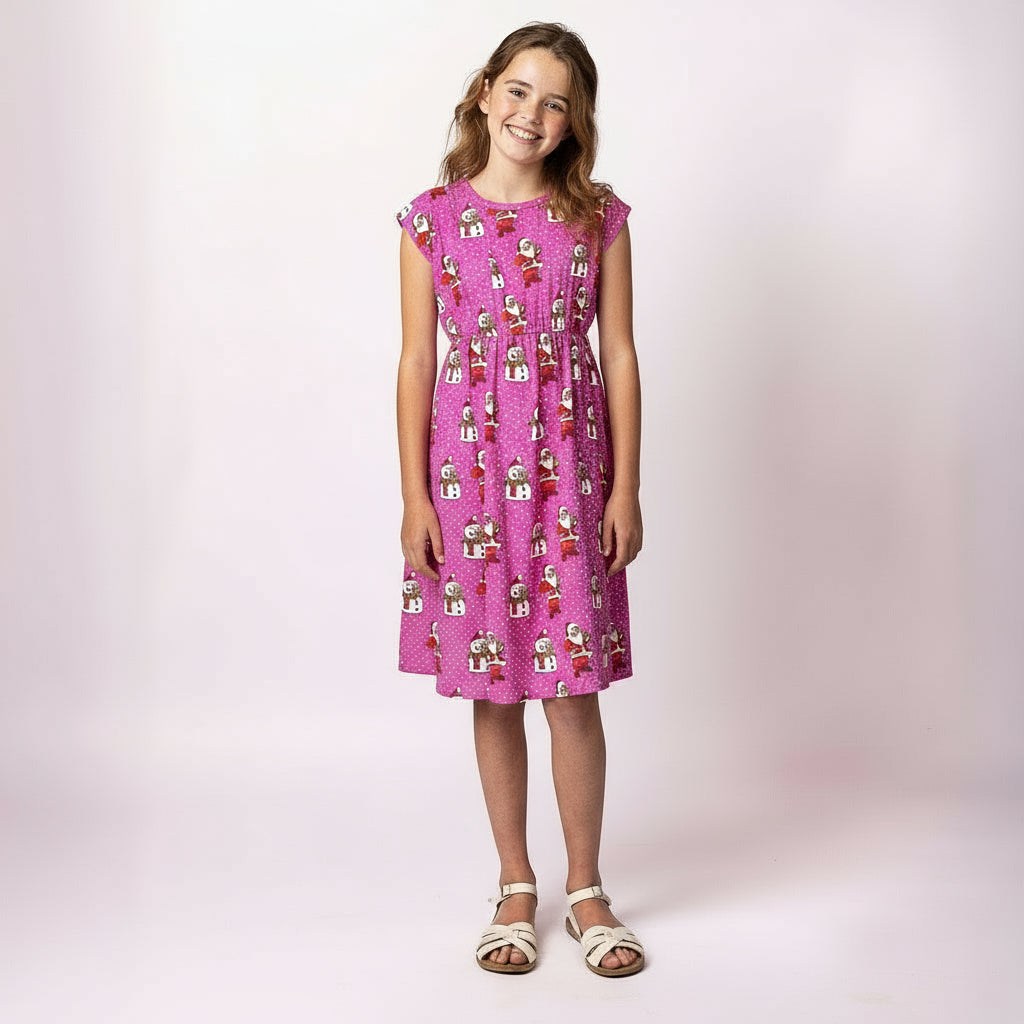 Girl wearing the Tropicool Holly Santa Polka Pink Child Dress, a fun pink Christmas dress with Santa and polka dot print, breathable summer fabric and family-matching design.