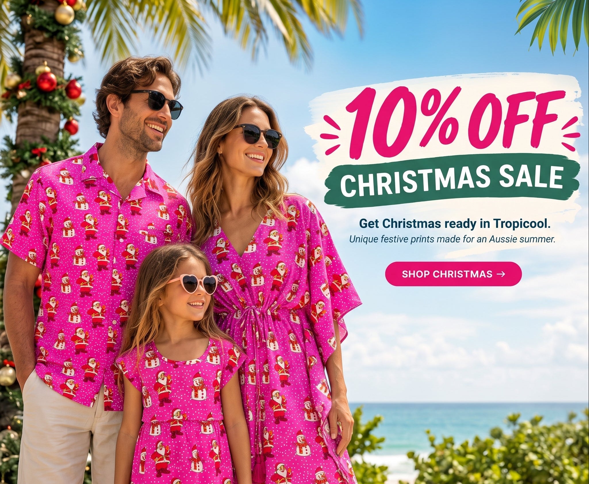 A family of four wearing matching bright pink tropical holiday shirts and dresses with a Santa Claus print, standing outdoors by the beach with palm trees, ocean, and a Christmas tree visible. Large sale text on the right reads '10% OFF Christmas Sale' with a 'SHOP CHRISTMAS ->' button.